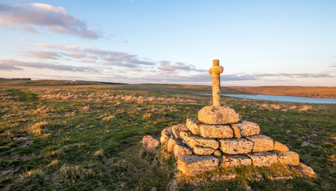 Randonnée sur le plateau de l'Aubrac : sentier et croix de chemin sous le soleil